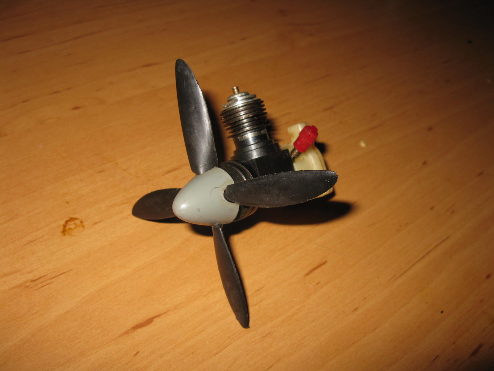 Volgens mij is dit een McCoy 0,8 cc, met vierblads prop.
Geïntegreerde tank, motor vermoedelijk afkomstig uit plastic lijnbestuurd model (geen bevestigings-ogen).
Kunststof carter, werkende veerstarter.
De vierblads prop met bijbehorende spinner is zeldzaam